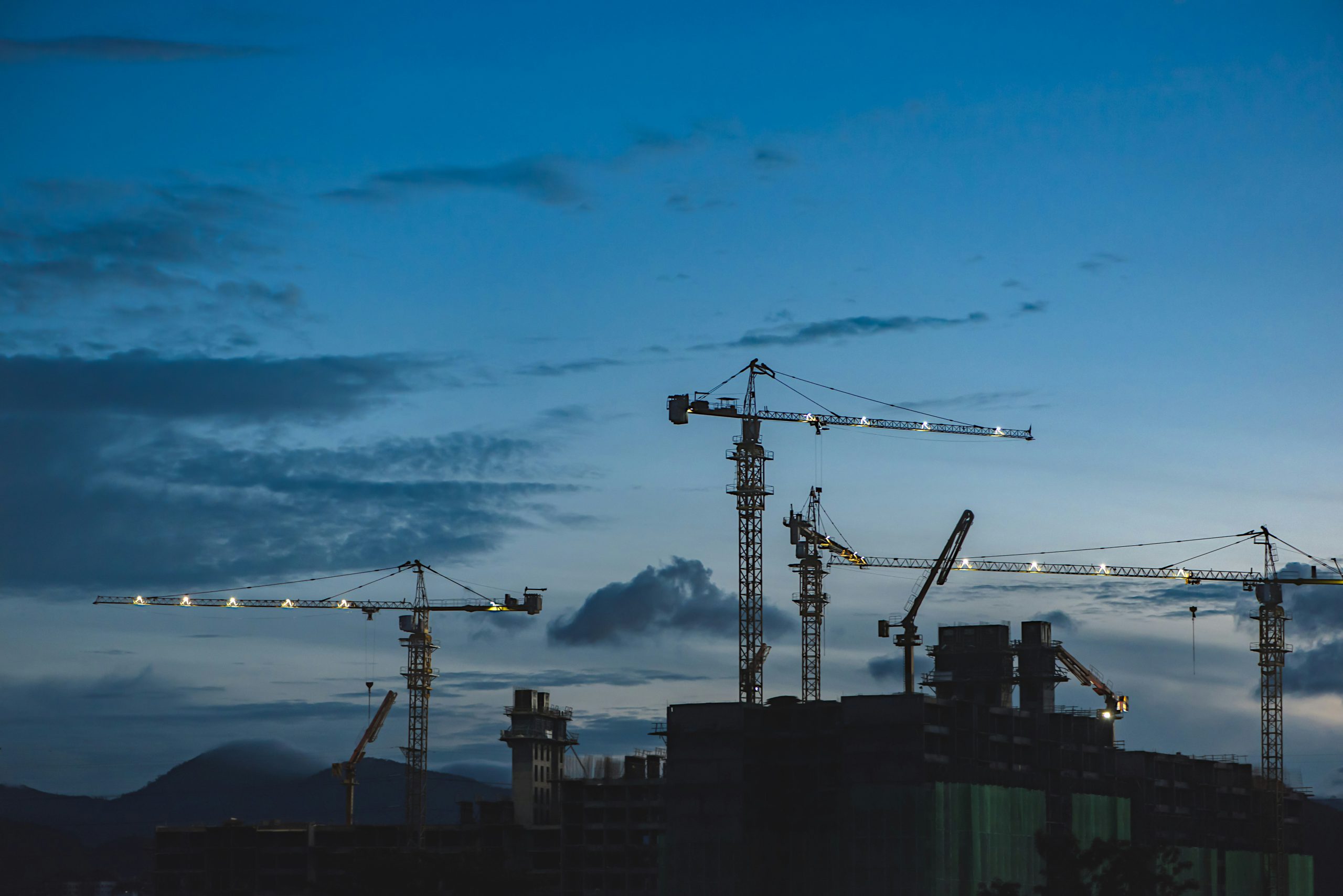 Construction site at dusk with multiple tower cranes in operation, highlighting large-scale infrastructure development. Ideal for showcasing civil engineering, and safe construction practices from Paul Feely & Associates, health and safety consultant