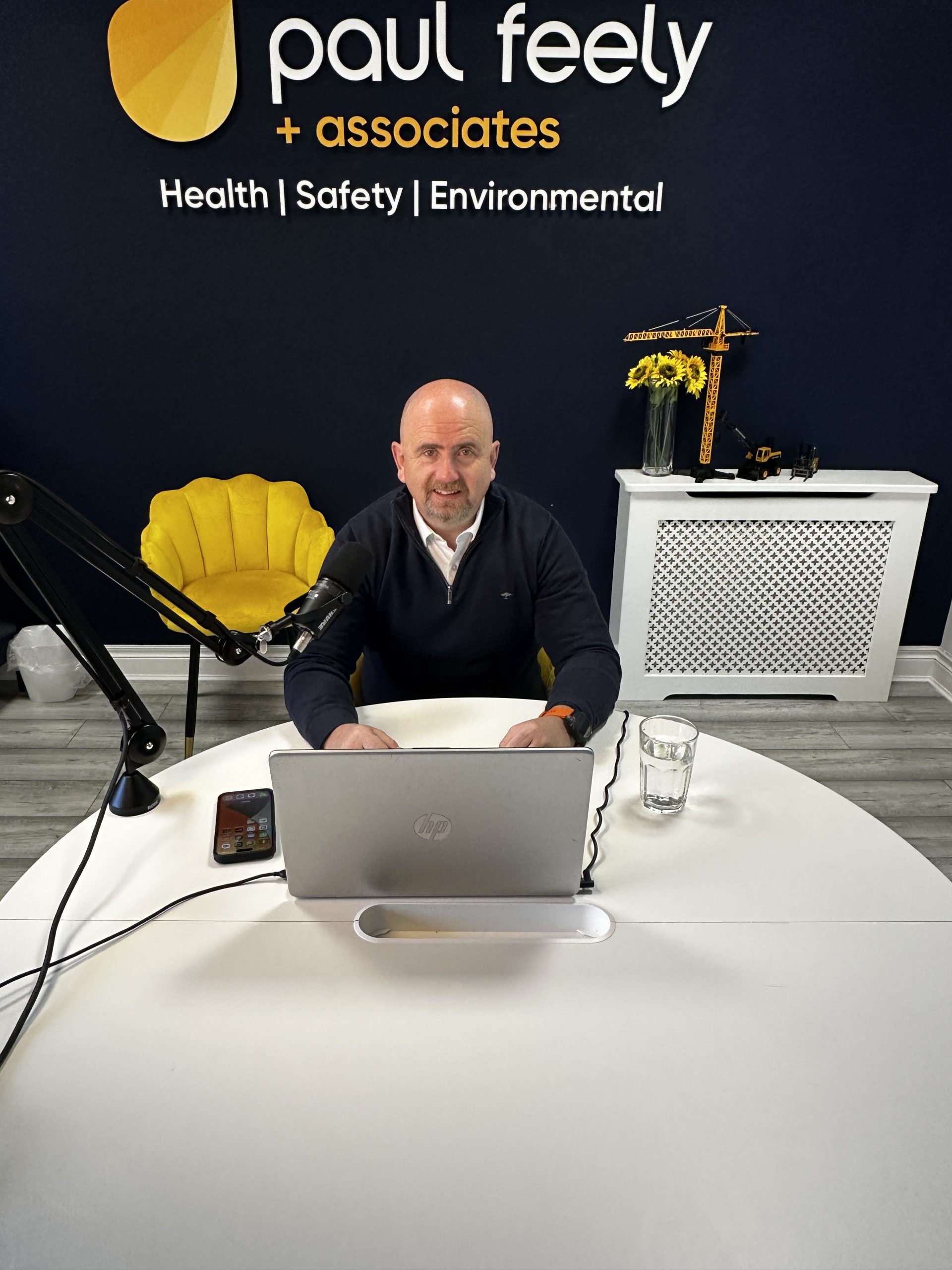 Paul Feely providing expert health and safety consultancy from office with branded company logo in background on a navy wall 